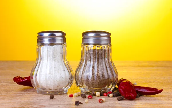 stock image Salt and pepper mills and spices on wooden table on yellow background