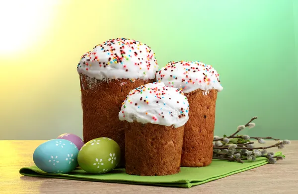 Hermosos pasteles de Pascua, huevos coloridos y ramitas de coño y sauce en la mesa de madera sobre fondo verde —  Fotos de Stock