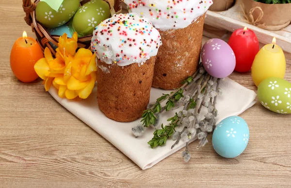 Красивые пасхальные торты, разноцветные яйца в корзине и свечи на деревянном столе — стоковое фото