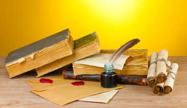 Old books, scrolls, feather pen and inkwell on wooden table on yellow background