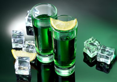 Two glasses of absinthe, lemon and ice on green background clipart