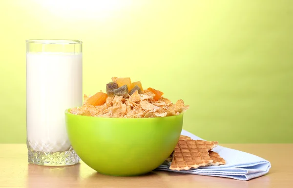 Tasty cornflakes in green bowl and glass of milk on wooden table on green background — Stock Photo, Image