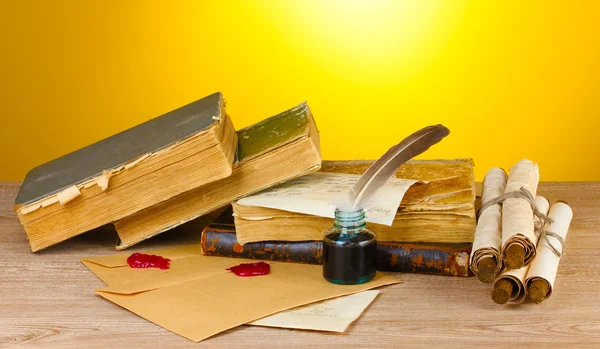 Old books, scrolls, feather pen and inkwell on wooden table on yellow background — Stock Photo, Image