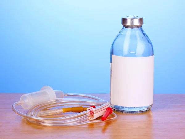 Бутылка внутривенных антибиотиков и пластиковых вливаний на деревянном столе на синем фоне — стоковое фото