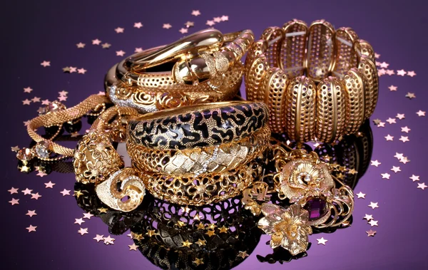 Krásné zlaté šperky na fialovém pozadí — Stock fotografie