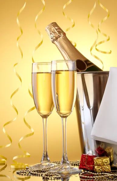 黄色の背景にシャンパンのグラスと氷バケットのシャンパンのボトル — ストック写真