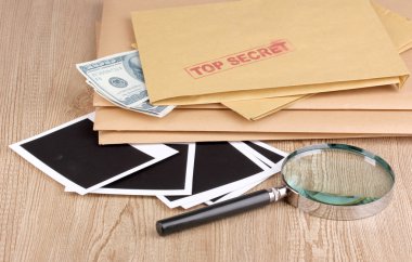 Envelopes with top secret stamp with photo papers and magnifying glass on wooden background clipart