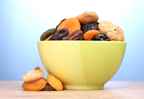 Dried fruits in green bowl on wooden table on blue background — Stock Photo, Image