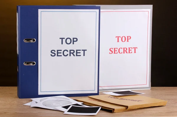 stock image Envelopes and folders with top secret stamp and photo papers with CD disks on wooden table on brown background