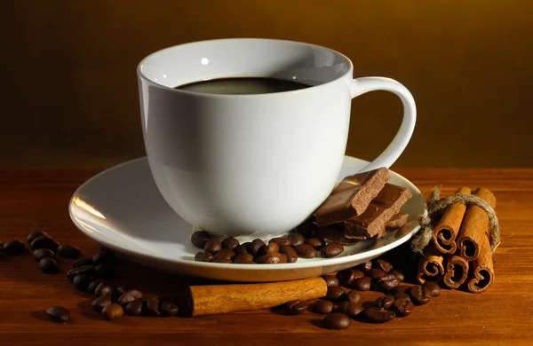 Tazza di caffè e fagioli, bastoncini di cannella e cioccolato su tavolo di legno su sfondo marrone — Foto Stock
