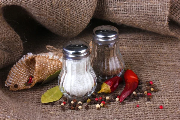 Salt and pepper mills and spices on burlap background — Stock Photo, Image