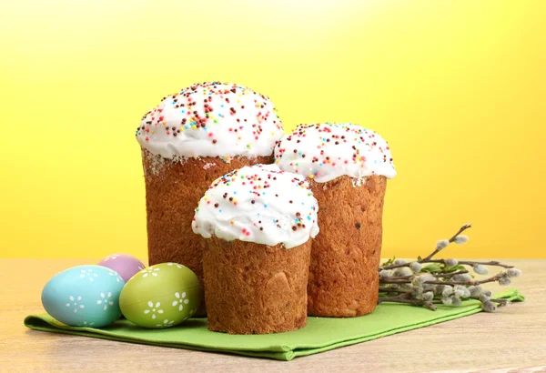 Mooie Pasen cakes, kleurrijke eieren en pussy-willow twijgen op houten tafel op gele achtergrond — Stockfoto