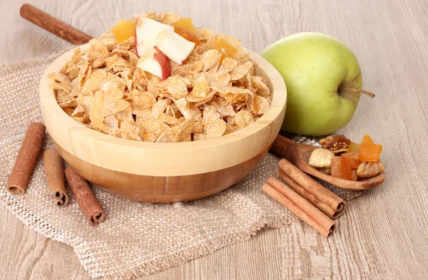 Tasty cornflakes in bowl with dried fruits, glass of milk and apple on wooden table — Stock Photo, Image