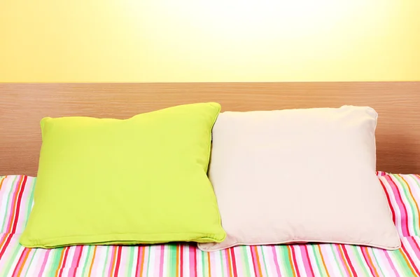Almofadas brilhantes na cama no fundo amarelo — Fotografia de Stock