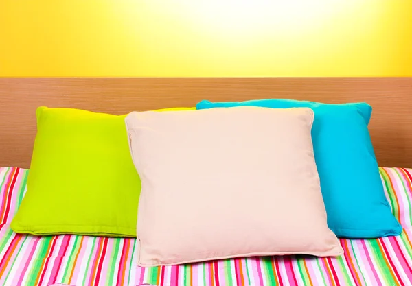 Heldere kussens op bed op gele achtergrond — Stockfoto