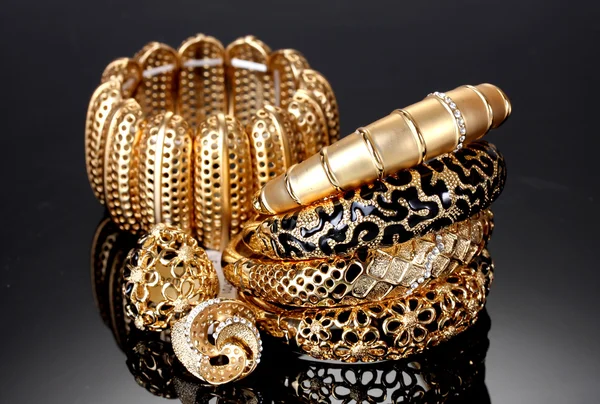 Belas pulseiras douradas e anéis no fundo cinza — Fotografia de Stock