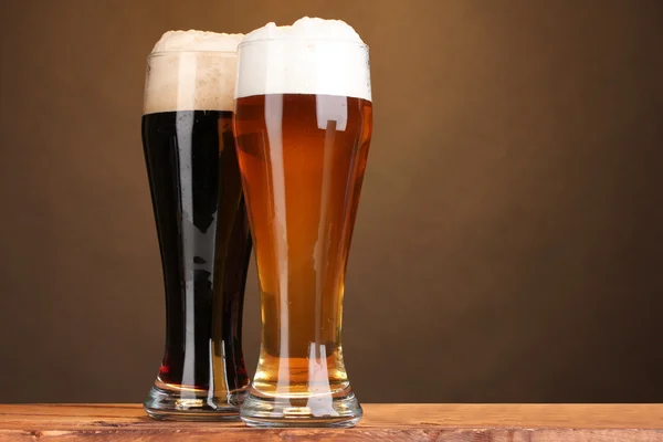 Czarny i złoty piwa w okularach na drewnianym stole na brązowym tle — Zdjęcie stockowe