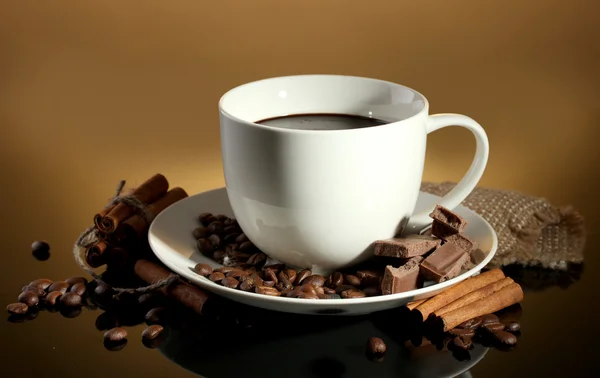 Kopp kaffe och bönor, kanelstänger och choklad på brun bakgrund — Stockfoto