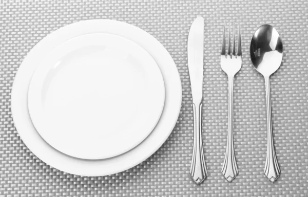 Bílé prázdné talíře, vidlička, lžíce a nůž na šedé ubrus — Stock fotografie