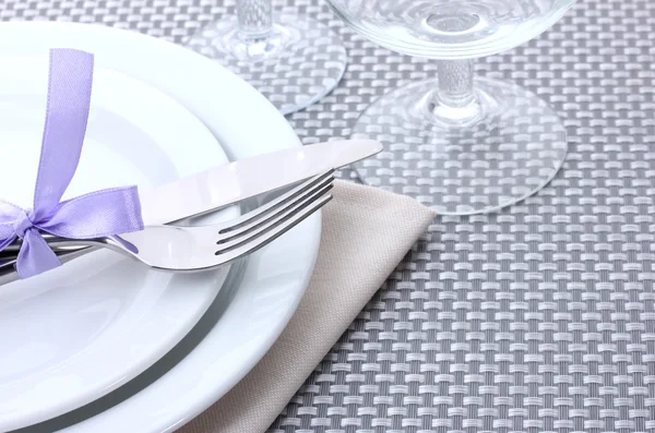 White empty plates, fork and knife tied with a ribbon and glasses on a grey tablecloth — Stock Photo, Image