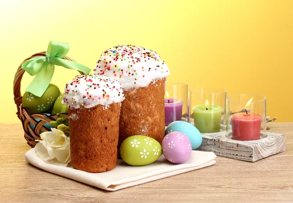 stock image Beautiful Easter cakes, colorful eggs in basket and candles on wooden table on yellow background