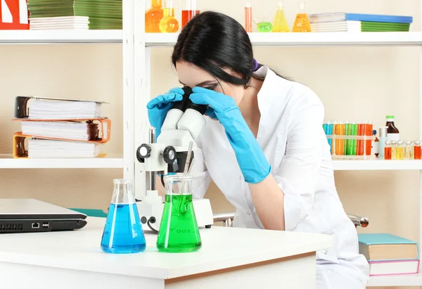 看着显微镜在化学实验室中的年轻女科学家 — 图库照片