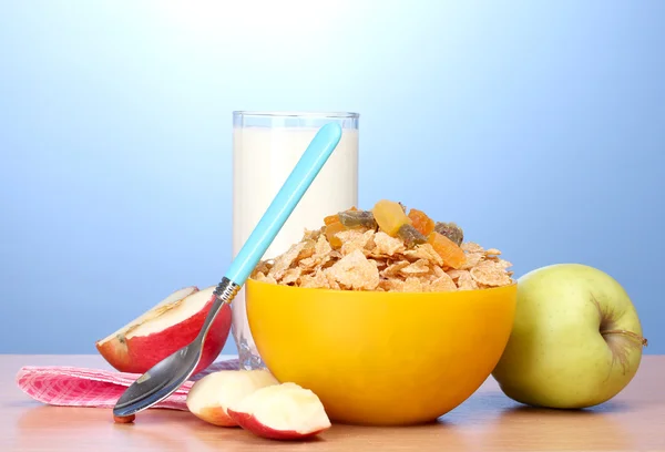Sabrosos copos de maíz en tazón amarillo, manzanas y vaso de leche sobre mesa de madera sobre fondo azul — Foto de Stock