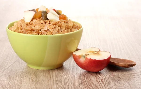 Leckere Cornflakes in Schüssel mit getrockneten Früchten und Apfel auf Holztisch — Stockfoto