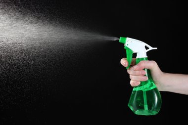 Hand holding spray bottle and spraying on black background clipart