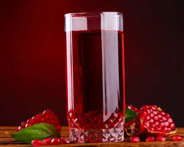 Pomergranato maduro y vaso de jugo sobre mesa de madera sobre fondo rojo — Foto de Stock
