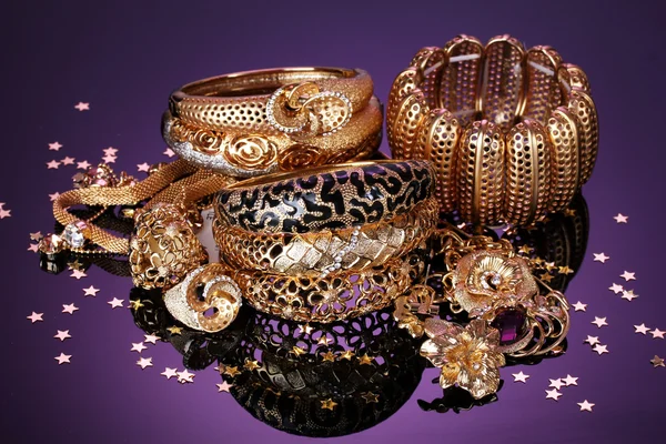 Belas jóias douradas em fundo roxo — Fotografia de Stock