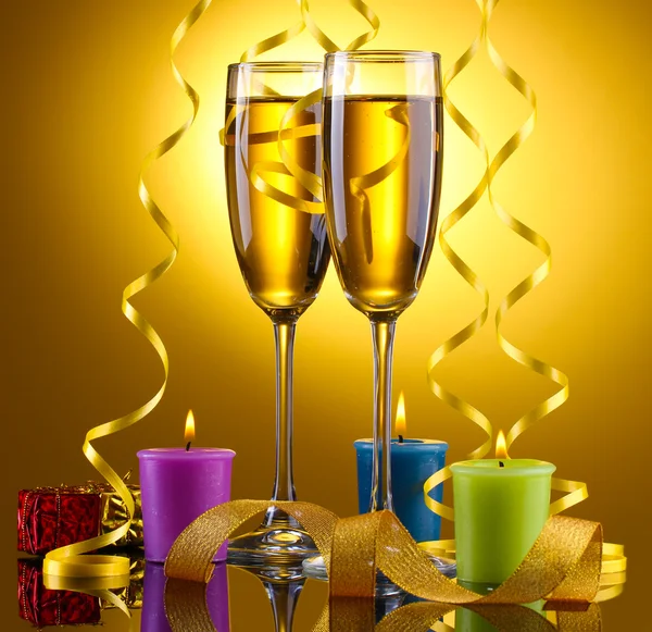 Pohár pezsgő, gyertyák, ajándékok és streamer, sárga háttér — Stock Fotó