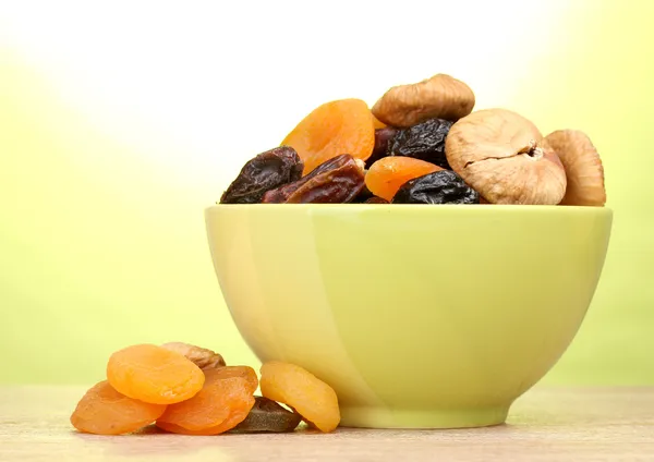 Dried fruits in green bowl on wooden table on green background