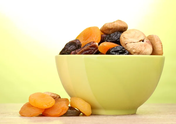 stock image Dried fruits in green bowl on wooden table on green background