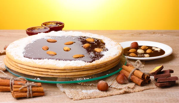 Kue di stand kaca dan kacang-kacangan di meja kayu dengan latar belakang kuning — Stok Foto