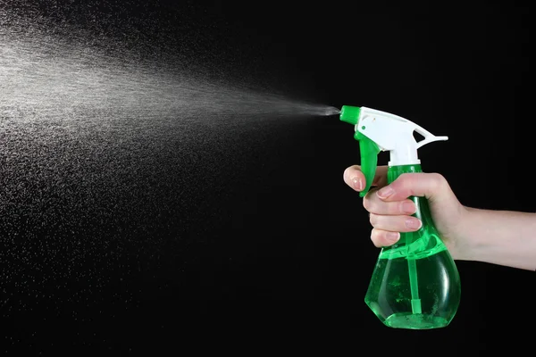 Hand holding spray bottle and spraying on black background — Stock Photo, Image
