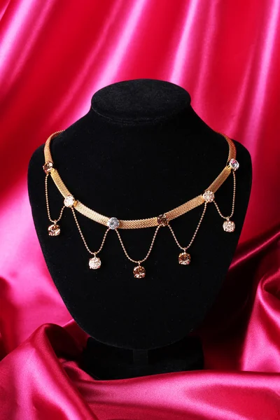 Hermoso collar de oro en el maniquí en tela de seda roja —  Fotos de Stock