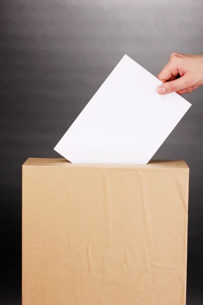 Mano con papeleta de votación y caja sobre fondo gris —  Fotos de Stock