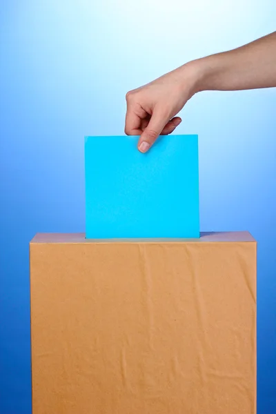 Рука с голосованием бюллетень и поле для голосования на синем фоне — стоковое фото