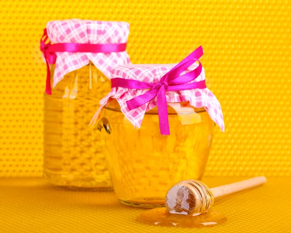 Jars of honey and wooden drizzler on yellow honeycomb background Stock Photo