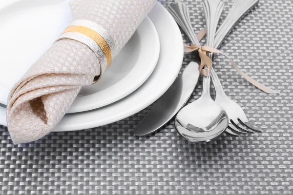 Bílé prázdné talíře, vidličku, lžíci a nůž svázané stuhou na šedé ubrus — Stock fotografie