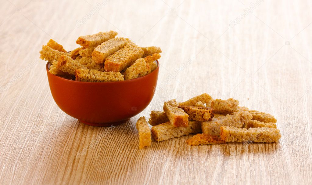 Appetizing rusks in bowl on wooden background