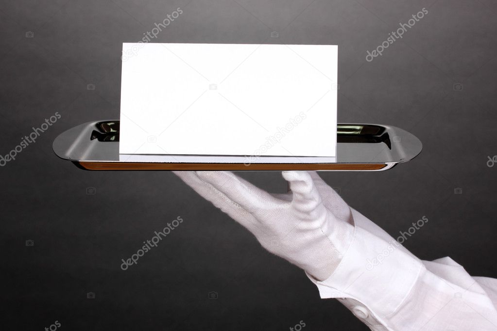 Hand in glove holding silver tray with blank card on grey background