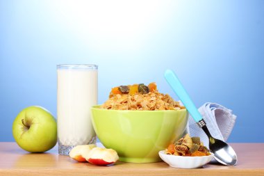 Tasty cornflakes in green bowl, apples and glass of milk on wooden table on blue background clipart