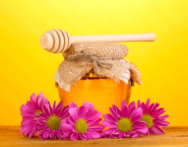 Sweet honey in jar with drizzler on wooden table on yellow background clipart