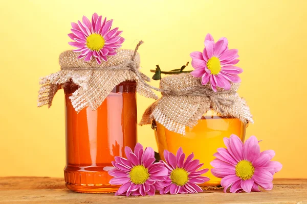 Sladký med ve sklenicích na dřevěný stůl na žlutém podkladu — Stock fotografie