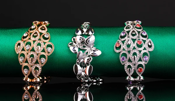 Três pulseiras elegantes no pano verde sobre fundo preto — Fotografia de Stock