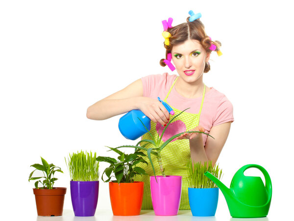 Beautiful happy young housewife sprays plants in flowerpots isolated on white