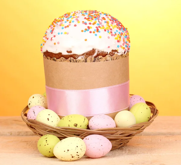 Beautiful Easter cake in basket with eggs on wooden table on yellow background — Stock Photo, Image