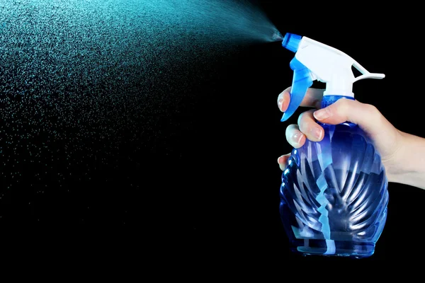 Mão segurando frasco de spray e pulverização em fundo preto — Fotografia de Stock